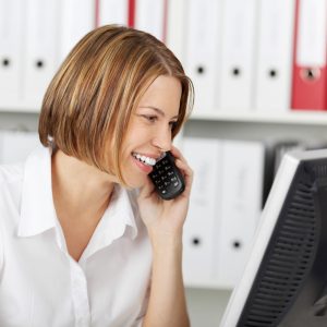 customer service skills: woman in while talking on the phone while looking at the computer