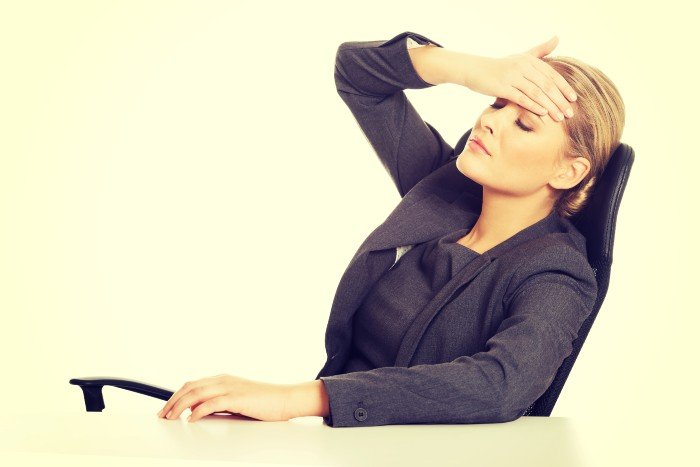 woman has her hand on her forehead as she leans back, seemingly under stress
