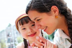 career in disability support: a little girl smiles at the camera while holding a lady's hand