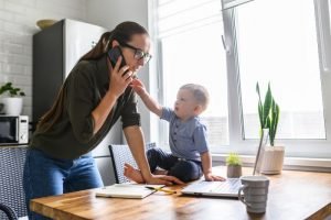 work from home: mum is on the phone with her toddler on the table