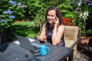 work-from-home: curly-haired woman is talking on the phone while working in the garden
