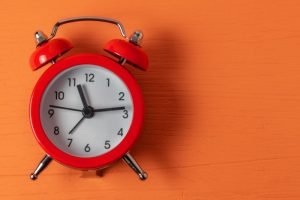 taking a break: a red alarm clock against a wooden board