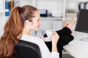taking a break: a woman with her feet up on her desk while holding a cup of coffee