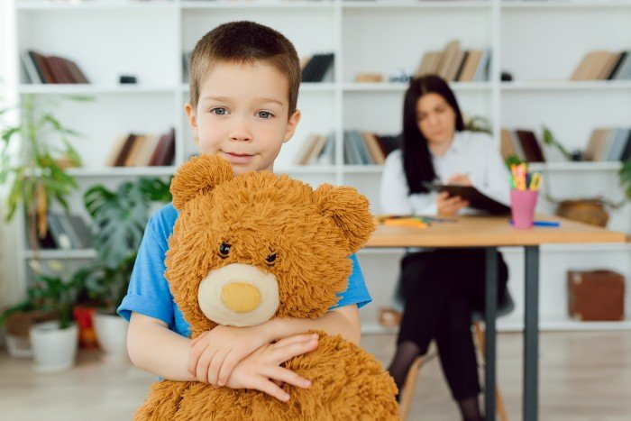 counselling children: a boy is holding a teddy bear with a child psychologist in the background